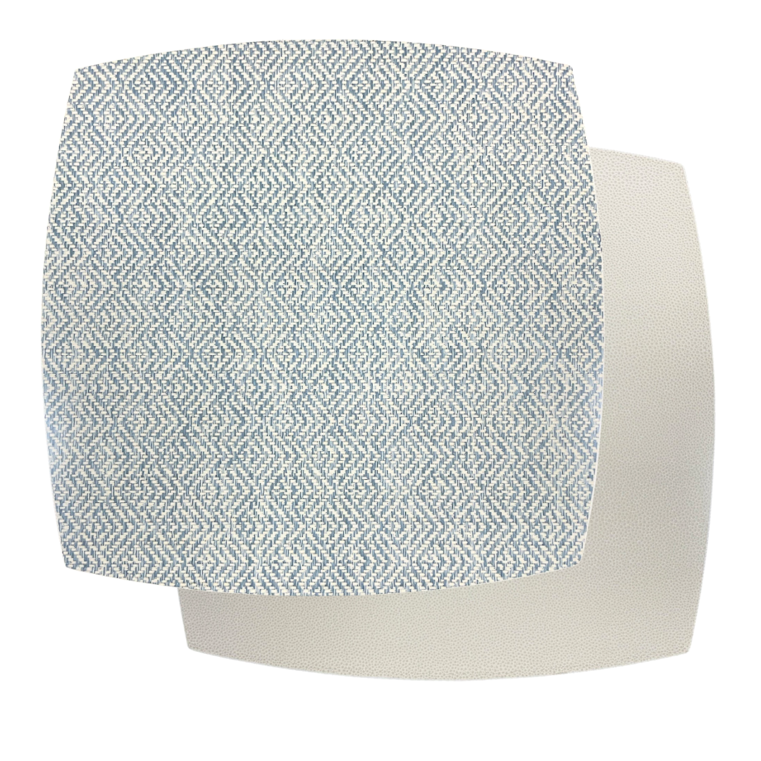 Two overlapping fabric swatches: the top features a blue and white geometric zigzag pattern, inspired by the Ellipse Reversible Placemat Set of 4 - Azure Eggshell by Julian Mejia, layered over a plain off-white textured swatch beneath.