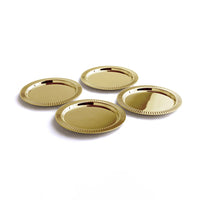 Four shiny, round gold-plated Striations Coasters by Anna New York are arranged closely together on a white surface, highlighting the elegant ridged edges and sophisticated design of this modern set of four, which comes with a matching holder.