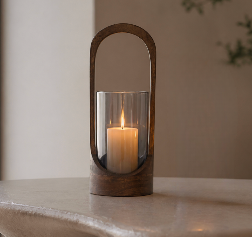 The Modesto Hurricane - Walnut by Sagebrook Home features a lit pillar candle in a glass holder with a sleek, oval walnut frame—ideal as modern decor for any space, shown on a light surface with a neutral background.