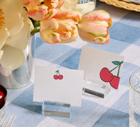 Two blank place cards with cherry illustrations stand in Dear Annabelle's Clara Place Card Holder Set of 6 - Clear on a blue and white checkered tablecloth, beside tulips in a silver vase, adding charm to this modern tablescape.
