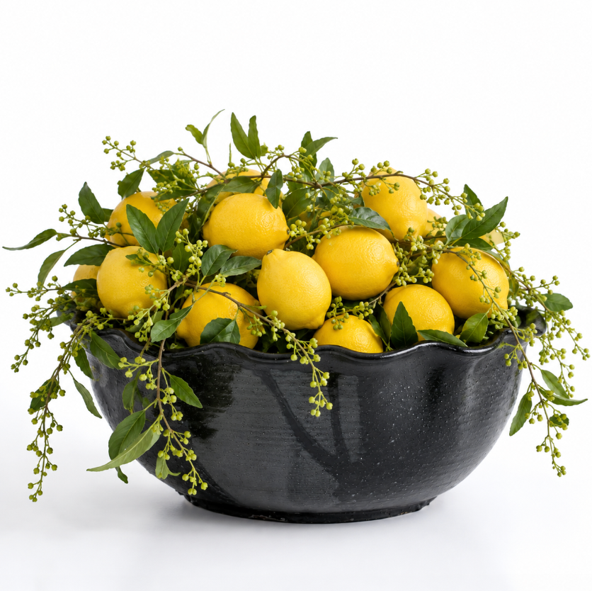 A Leona Bowl - Marina by CDMX / MASA TALLER, crafted from black ceramic and filled with fresh yellow lemons and green leafy sprigs, creates a striking decorative accent against a white background for any space.
