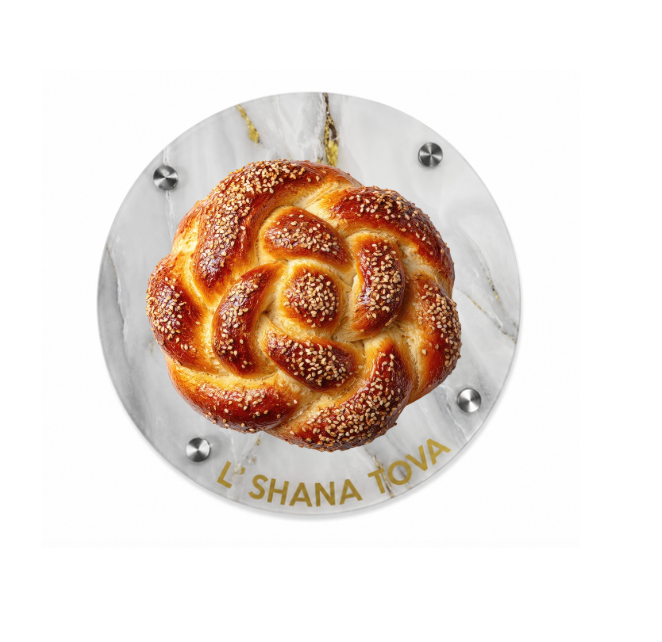 A round, braided challah topped with sesame seeds rests on the Eye Candy Round Challah Board in White/Gold/White, featuring “LSHANA TOVA” elegantly written in gold letters at the bottom—making it the perfect centerpiece for your holiday table.