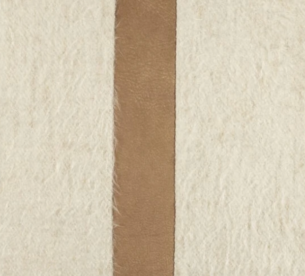The Bruno Pillow - Bisque & Camel from Moss Studio features a vertical camel leather contrast band running down the center of its textured, off-white, hairy surface, elegantly dividing it into two sections and adding a touch of luxury perfect for modern interiors.