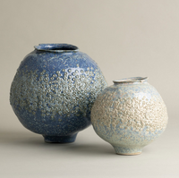 Two spherical textured ceramic vases, including a larger Briar Light Blue Vase by FlowDecor Inc. and a smaller off-white vase, both with bumpy surfaces, sit side by side against a plain, light background.