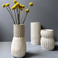 Three unglazed porcelain Chain Bottle Vase Cream 11″ pieces featuring a textured, chain-link pattern, with the tallest holding a bouquet of yellow billy button flowers.