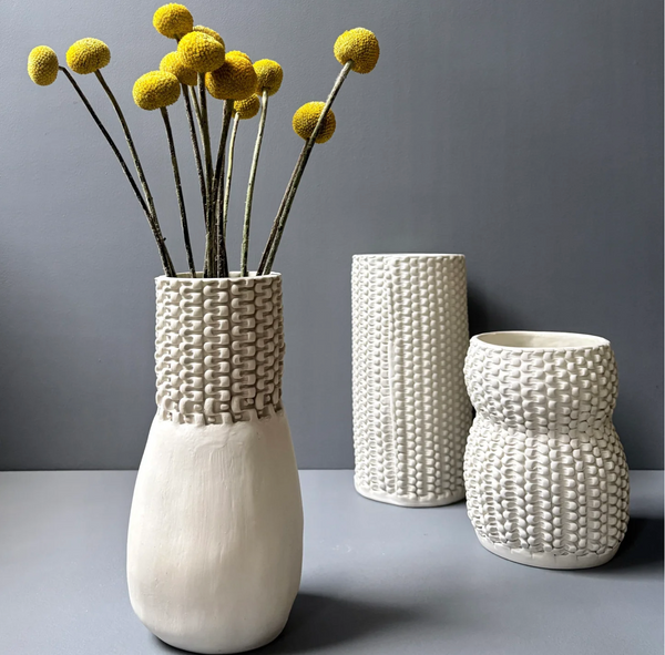 Three unglazed porcelain Chain Bottle Vase Cream 11″ pieces featuring a textured, chain-link pattern, with the tallest holding a bouquet of yellow billy button flowers.