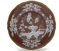 A round, brown porcelain plate from the Ginori 1735 Oriente Italiano Castagna set features a scalloped gold rim and intricate white floral and basket patterns at the center and along the edges.