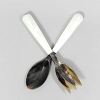 The Nashi Home Vera Horn Server Set features a spoon and fork with marbled handles crossed on a light gray background. The handcrafted pieces display unique brown, black, and cream tones with distinctive streaks.