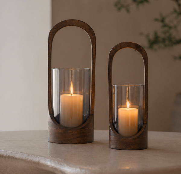 Two Modesto Hurricane - Walnut candle holders by Sagebrook Home, one tall and one short, feature oval walnut frames with glass inserts. Placed on a light surface, they’re perfect for adding modern style to your home decor.