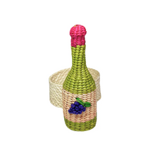 The Coro Cora Wine Napkin Ring Set of 4 - Pink features handwoven straw-like material with a pink top, green neck and base, cream middle, and purple grape detail—artisan table decor handcrafted in Colombia. Cream woven band shown in background.