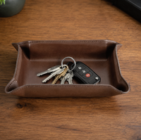 The Graphic Image Leather Valet Tray Medium rests on a wooden surface, providing an ideal men's organizer for accessories like a black car key fob and metal house keys.