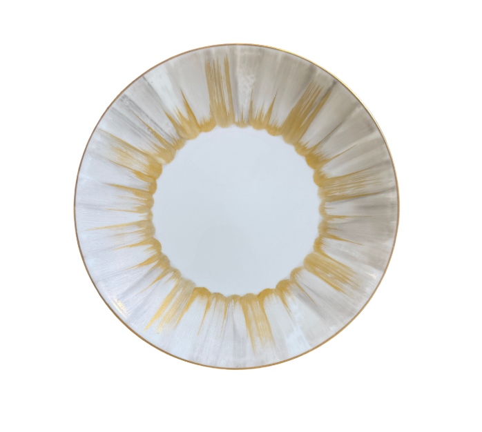 The Marie Daâge Panache plate by Marie Daâge is a round white Limoges porcelain piece with a decorative rim of gold and gray brushstroke patterns radiating inward.