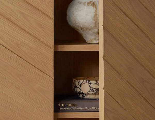 A wooden shelf displays the Emperor Purple Marble Bowl by Currey & Company, a sculptural piece crafted from striking purple marble, accompanied by a round white vase and a partially visible copy of *The Shell: Five Hundred Million Years of Inspired Design* on the lower shelf—an elegant blend of natural stone decor and refined design.