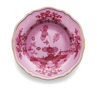 A pink porcelain bowl from the Oriente Italiano Porpora collection by Ginori 1735, featuring scalloped edges, gold trim, and intricate red floral and decorative patterns inspired by elegant chinoiserie motifs.