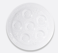 Introducing the Bernardaud Louvre Dinnerware Seder plate—a white, round piece featuring seven decorative, indented sections arranged in a circle and adorned with ornate floral patterns around the edges, inspired by the elegance of French architecture.