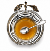The Pomona Apple Bowl by Mary Jurek, crafted in a gleaming silver apple shape and shown filled with honey with a spoon resting inside, photographed from above on a white background, makes an elegant holiday serving bowl perfect for your Rosh Hashanah table.