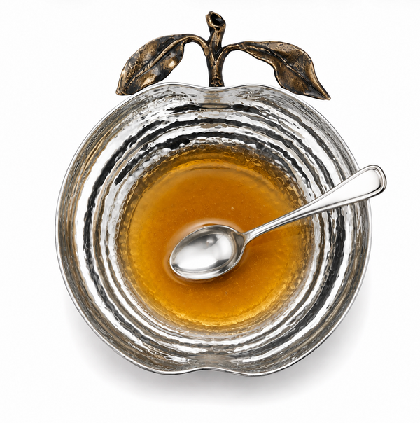 The Pomona Apple Bowl by Mary Jurek, crafted in a gleaming silver apple shape and shown filled with honey with a spoon resting inside, photographed from above on a white background, makes an elegant holiday serving bowl perfect for your Rosh Hashanah table.