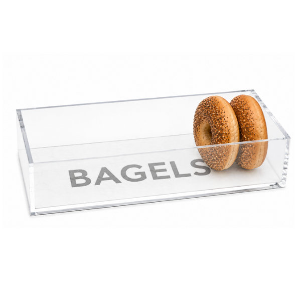 A clear, rectangular Eye Candy Bagel Tray labeled “BAGELS” holds two sesame bagels inside and is positioned near the right side of the food-safe container—making it a thoughtful gift for any breakfast lover.