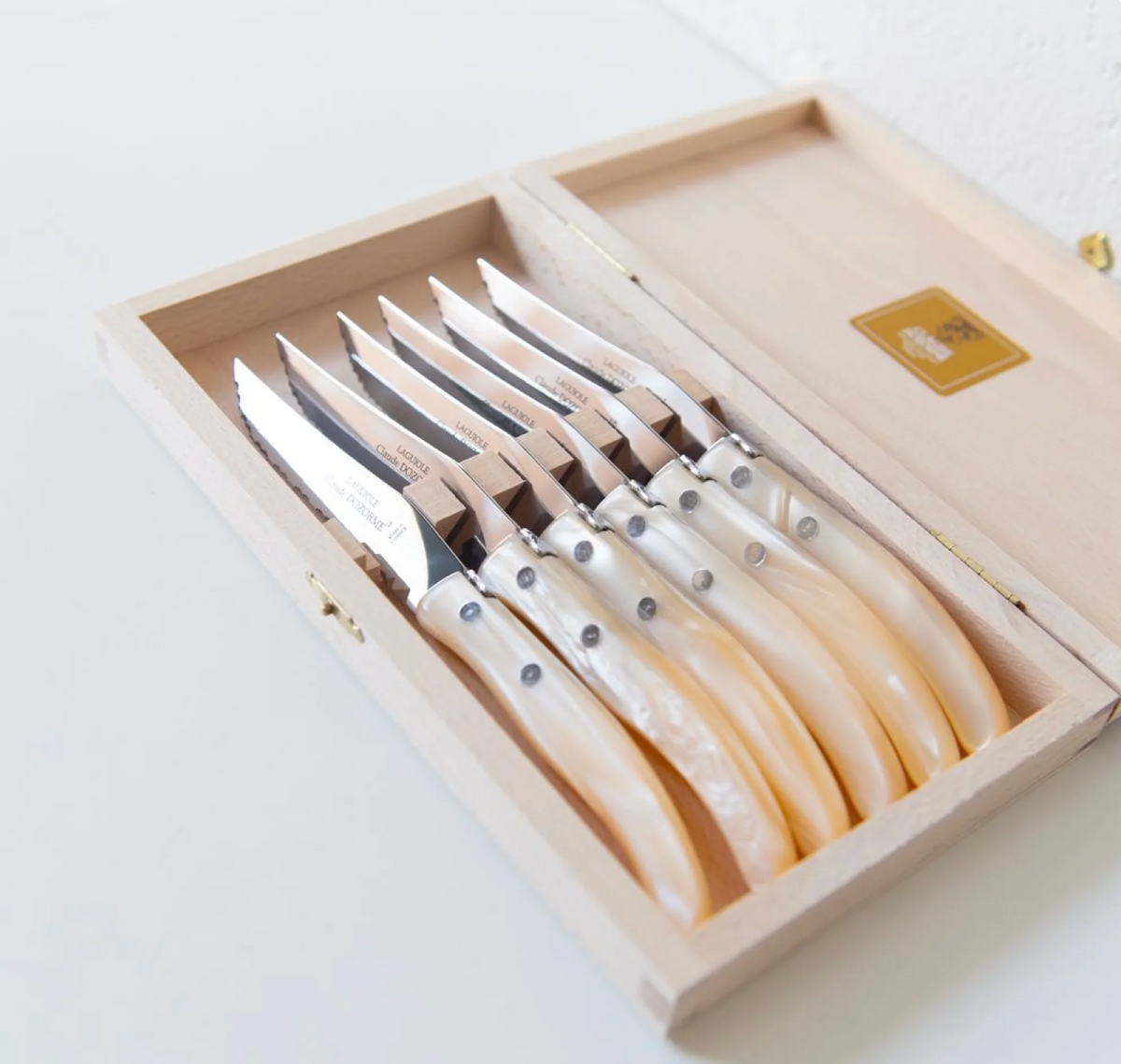 A wooden box containing the Berlingot Steak Knives Set of 6 by Claude Dozorme, each pearl-handled knife showcasing a gleaming blade, expert craftsmanship, and distinctive rivets on the handle, all neatly organized inside.
