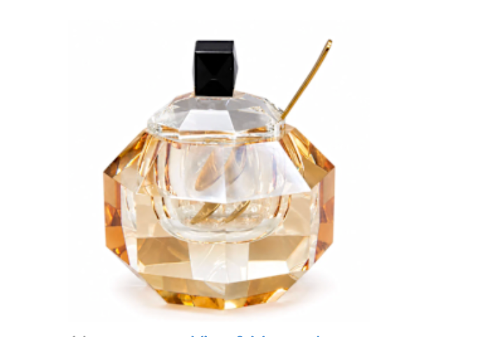 Certainly! Here’s a rewritten version of your sentence using the provided product data: The BT-Shalom Crystal Honey Jar with Spoon in amber and black features a faceted crystal design inspired by the traditional apple shape, adorned with a gold stem and topped with a sleek black square cap. Reminiscent of the gleaming honey dishes gracing Yom Tov tables, this jar reflects light beautifully—its amber and clear tones perfectly capturing the spirit of Rosh Hashanah.