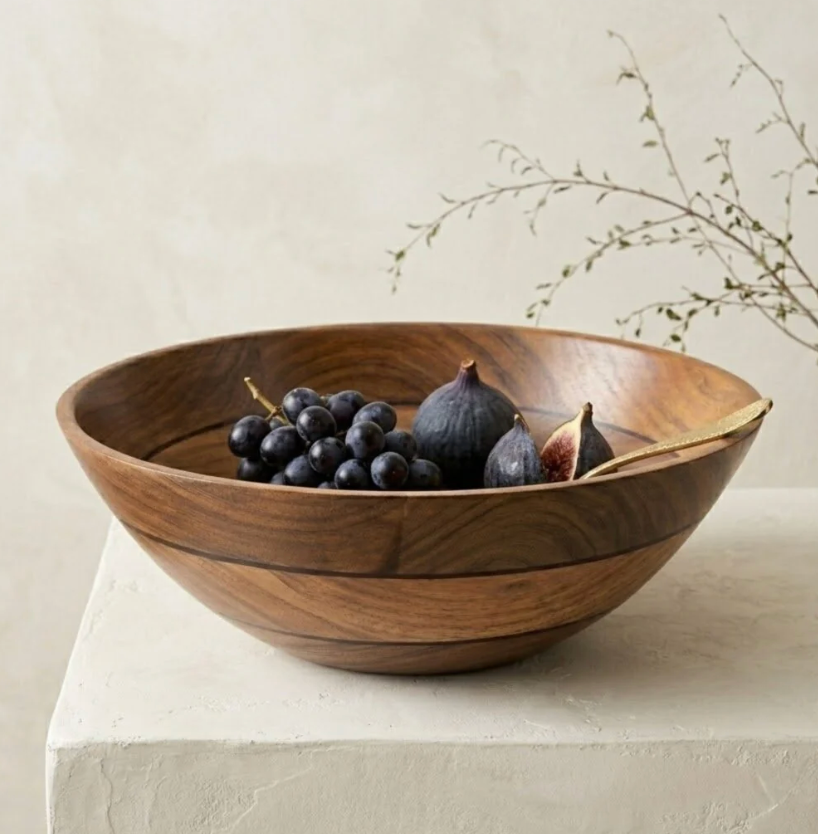 The Volare Large Serving Bowl by Be Home, filled with black grapes and figs, sits on a white stone surface. A gold spoon rests inside the bowl. In the background, a sprig of greenery is set against a neutral wall.