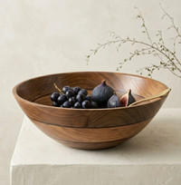 The Volare Large Serving Bowl by Be Home, filled with black grapes and figs, sits on a white stone surface. A gold spoon rests inside the bowl. In the background, a sprig of greenery is set against a neutral wall.