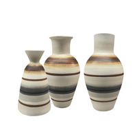 Elevate your space with the Carina Vase- Large by Mood Dekor—an artisanal ceramic piece featuring a wide body and narrow neck, adorned with horizontal brown, beige, and black stripes on a white background. Its modern earthy design adds a stylish touch to any room.
