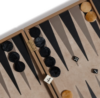 The Gene Leather Backgammon - Taupe by Zodax is a handcrafted set that features black and brown checkers, two dice showing 2 and 6, and a doubling cube displaying the number 4. The luxury game board is artfully presented at an angle, with part of its hinge visible for an added touch of elegance.
