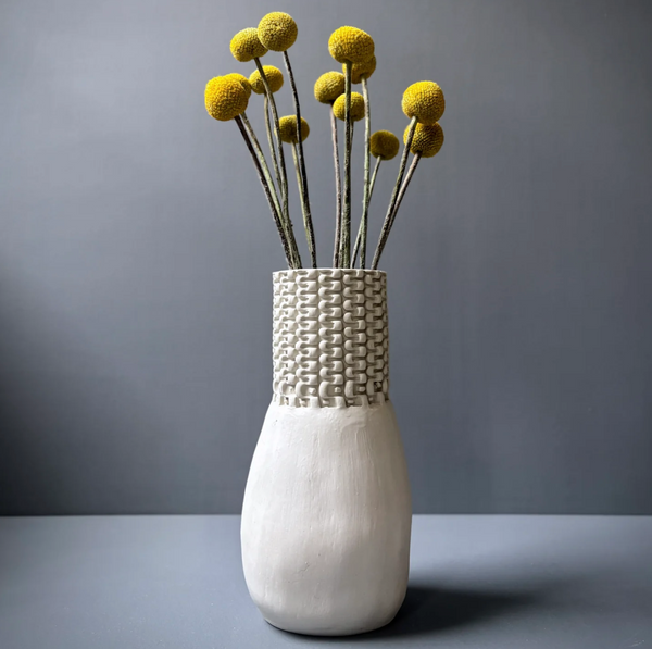Cream-colored Chain Bottle Vase Cream 11″ by CYM Warkov Ceramics, an unglazed porcelain vase with a textured chain-link pattern neck, holding a bouquet of yellow billy button flowers.