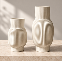 Two off-white, unglazed porcelain CYM Warkov Ceramics Frame Vase Cream vases with vertical ridged textures sit on a stone surface.