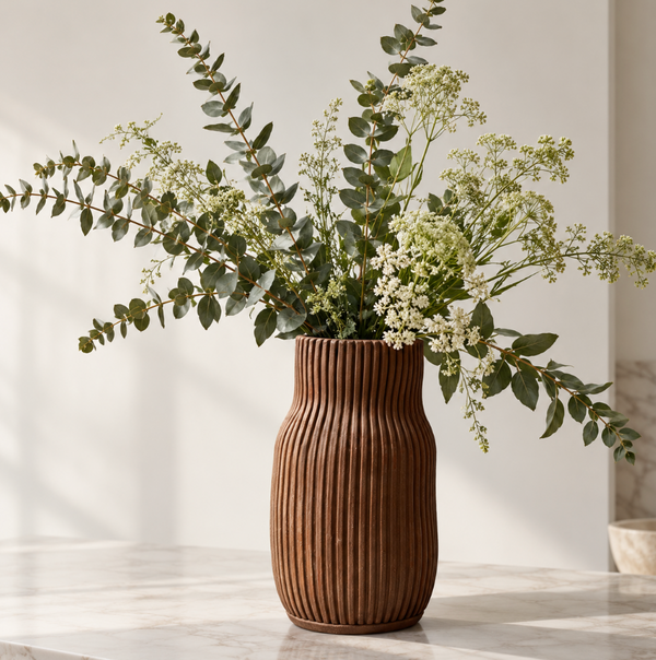 A CYM Warkov Ceramics Stoneware Bottle Vase - Dark Brown filled with eucalyptus branches and white flowers.