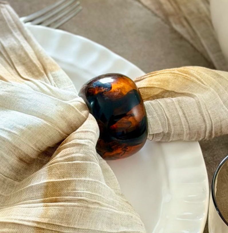 A spherical Sphere Napkin Ring Set of 4 - Tortoise holding a folded beige napkin on a white plate.