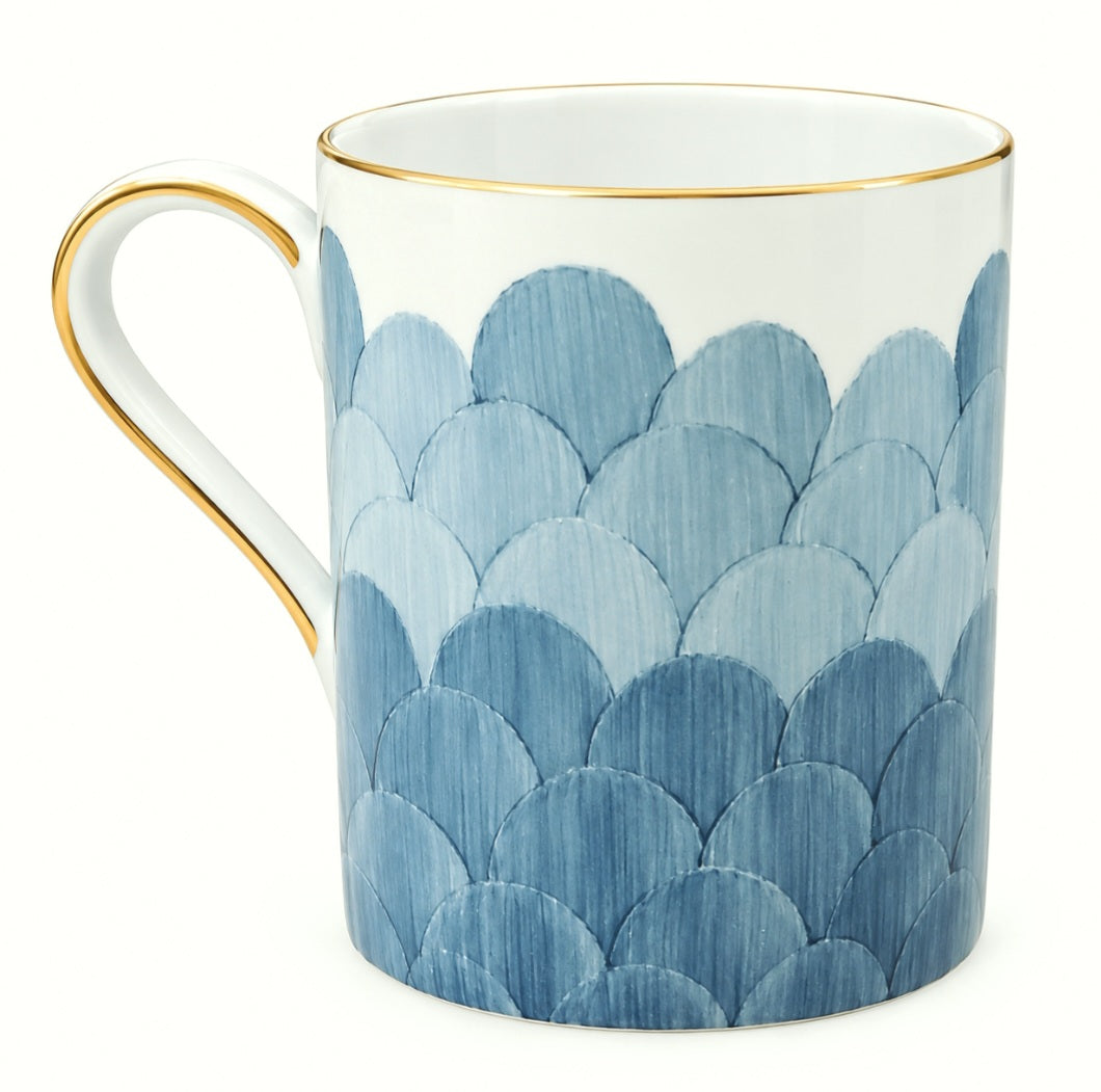 The Marie Daâge Cercle D’Ecailles Gold Filet by Marie Daâge is a white ceramic mug with a gold rim and handle, featuring a blue scallop pattern that wraps around the lower portion, inspired by classic French tableware.