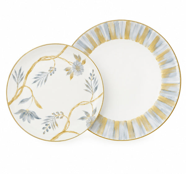 Two Marie Daâge Bouquet De Vie 1 dinnerware plates, one with hand-painted blue flowers and vines, the other with a gold and blue striped border, both featuring gold rims.