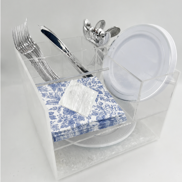 The Eye Candy Posh Swivel Silverware Caddy in white holds silver forks, knives, and spoons with white plastic plates, blue and white floral napkins, and a small clear packet.