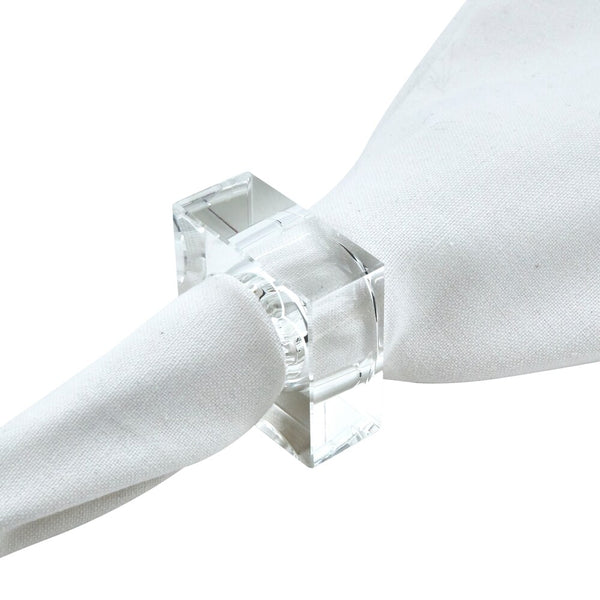 A white cloth napkin is elegantly secured by the Tizo Crystal Cube Napkin Ring, a clear, square-shaped acrylic accent from the Crystal Cube Napkin Ring Set of 4, creating a modern and sophisticated look against a plain white background.