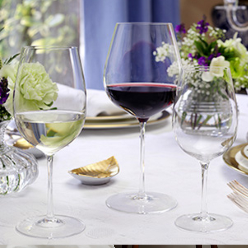 Three lightweight Starr Stemware wine glasses by William Yeoward—one with white wine, one with red, and one empty—sit on a white tablecloth. In the background are a vase of flowers and elegant tableware.