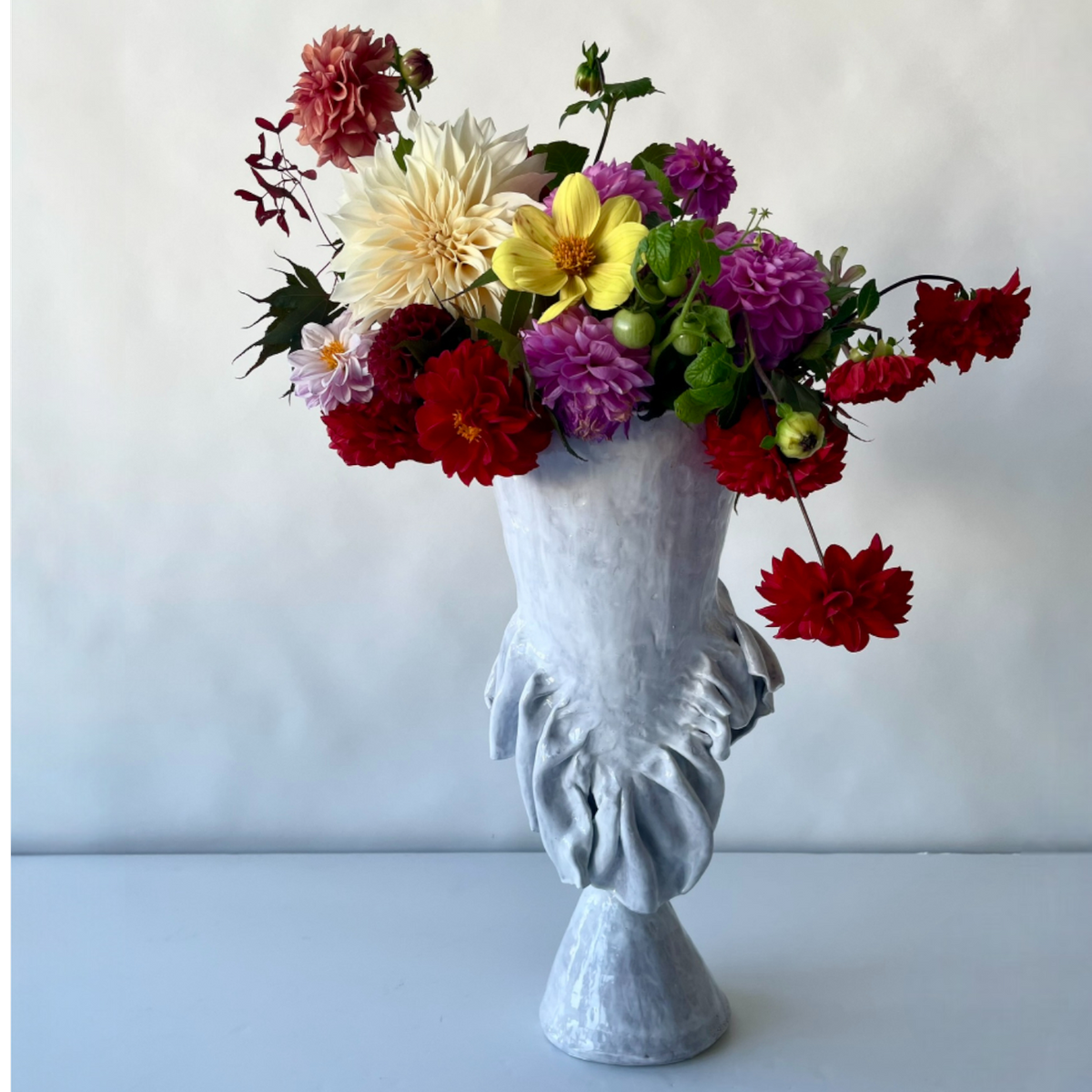 A vibrant mix of dahlias fills the "Without Her Trumpet Vase" by Ellen Robinson Studio, a hand-formed white-glazed vessel elegantly shaped as a classical bust.