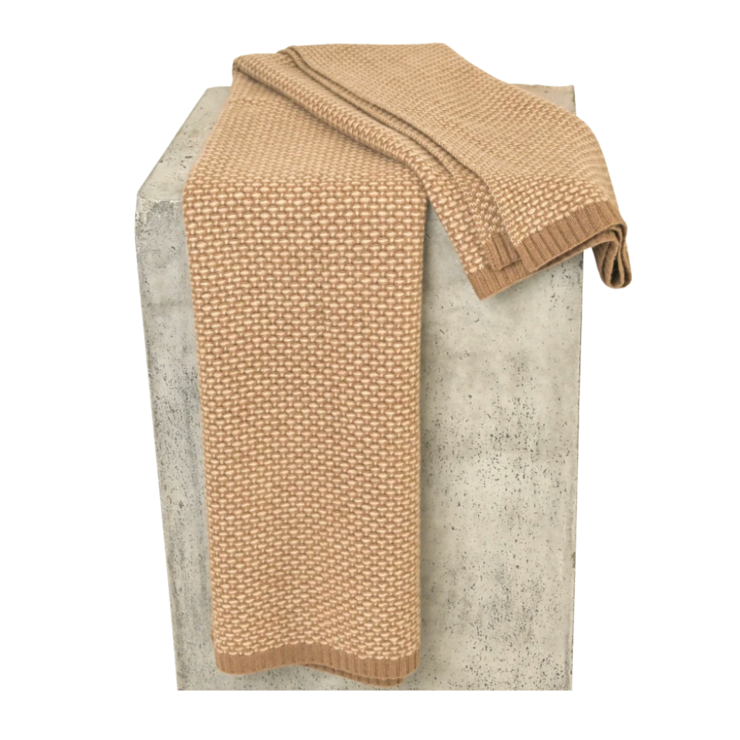 A Taiga Throw Gobi & Sand by Hangai Mountain Textiles, featuring a beige, textured knit, is draped over a rectangular gray concrete pedestal against a white background.