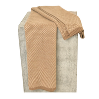 A Taiga Throw Gobi & Sand by Hangai Mountain Textiles, featuring a beige, textured knit, is draped over a rectangular gray concrete pedestal against a white background.