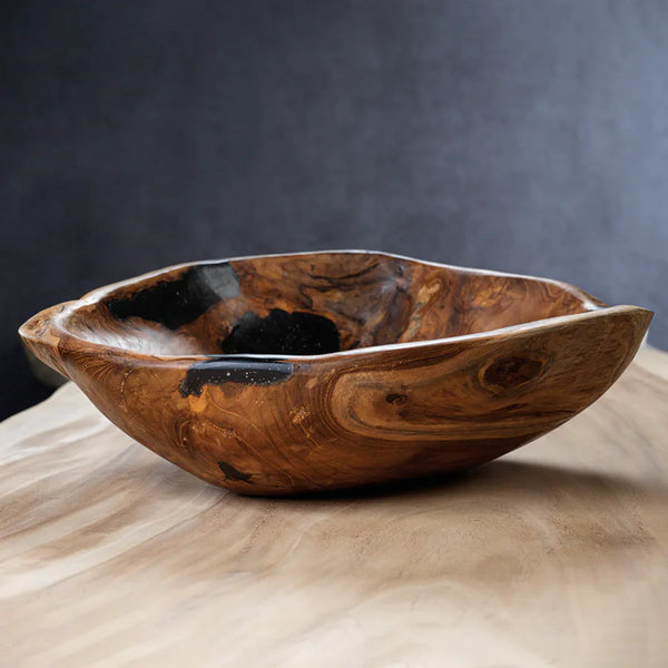 The Zodax Kenya Teakwood Bowl - 20" features a handcrafted, rustic design with natural, uneven edges and dark resin accents—perfect as home décor or a decorative fruit bowl on any light wooden surface.
