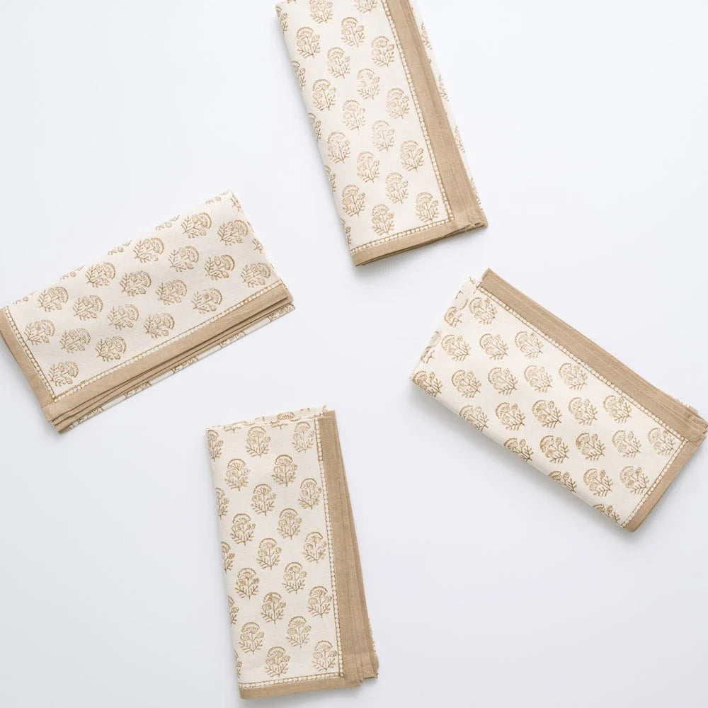 The Anika Napkin Set of 4 by Pomegranate features cream-colored napkins with a light brown floral block print and beige borders, neatly folded to highlight their artisan craftsmanship and timeless elegance.
