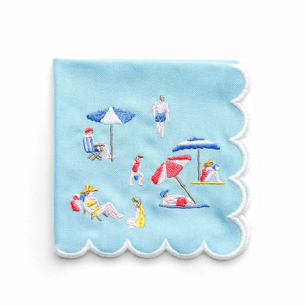 The Day At The Beach Cocktail Napkin set of 4 by Pomegranate features light blue napkins with scalloped edges and embroidered beach scenes—ideal for adding playful, coastal charm to your next gathering.