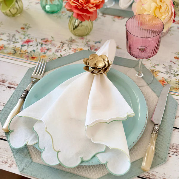 A pastel table setting with a blue plate, Bodrum Firenze Napkin Set of 4 - Ice Blue scalloped napkin held by a gold floral ring, vintage-style cutlery, pink glass, topped off with a floral runner and vases of colorful blooms.