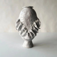 The Without Her Vase by Ellen Robinson Studio is hand-formed with a glossy light gray finish, showcasing organic wavy protrusions on its rounded body and narrow base, set against a plain, light background.