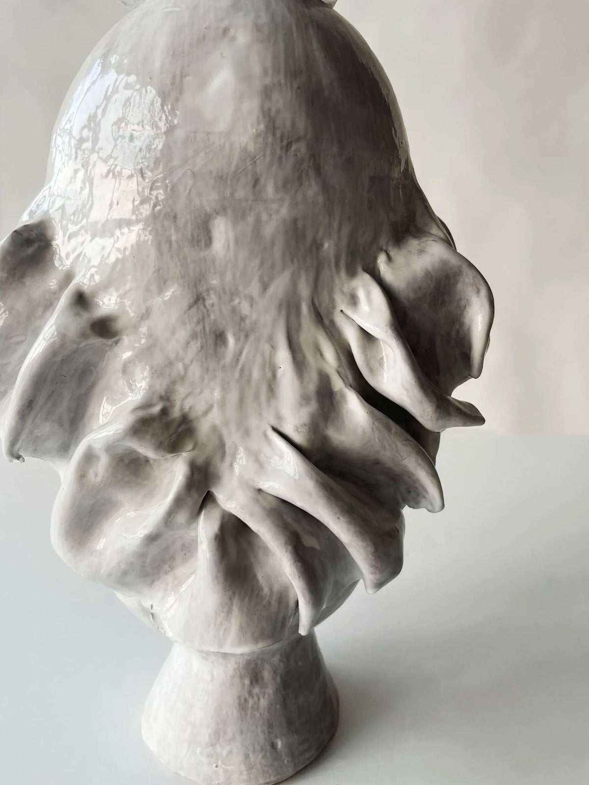 The Without Her Vase by Ellen Robinson Studio is a glossy, abstract ceramic sculpture with organic, flowing shapes and ruffled edges, finished in a sleek white glaze and displayed on a round base against a plain light background.