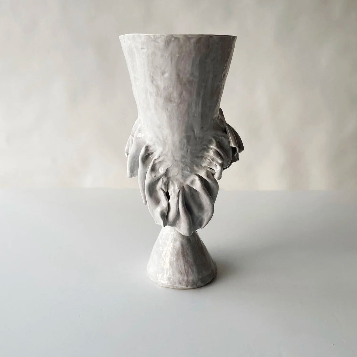 The Without Her Trumpet Vase by Ellen Robinson Studio features a textured, light gray hand-formed design with an abstract, sculpted leaf motif on the front, set against a plain, softly lit background.
