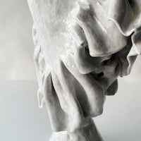Close-up of the Without Her Trumpet Vase by Ellen Robinson Studio—a glossy, hand-formed piece with smooth curves and layered folds in reflective white glaze. The plain background remains softly out of focus.