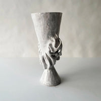 The Without Her Trumpet Vase by Ellen Robinson Studio features a sculpted, hand-formed gray design with a flared rim, textured surface, and abstract pattern around the midsection, set against a plain light background.