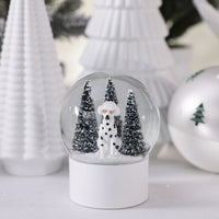 A Zodax Dalmation Snow Globe featuring a dog wearing orange sunglasses, standing in front of two pine trees on a snowy base.